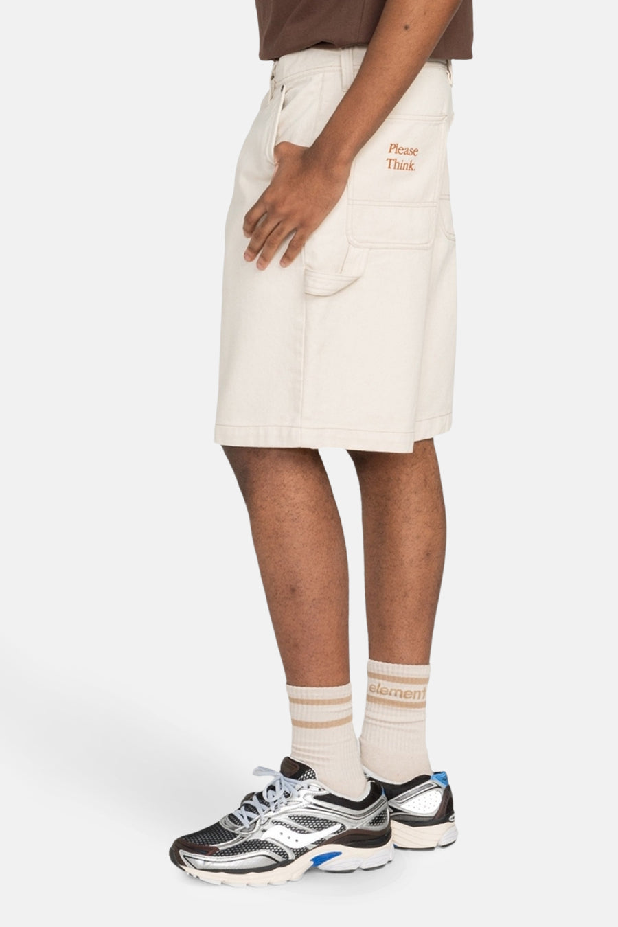 Crème court d'ELEMENT, avec un texte brodé et des poches cargo, porté avec des chaussettes rayées et des baskets argentées en vue latérale.