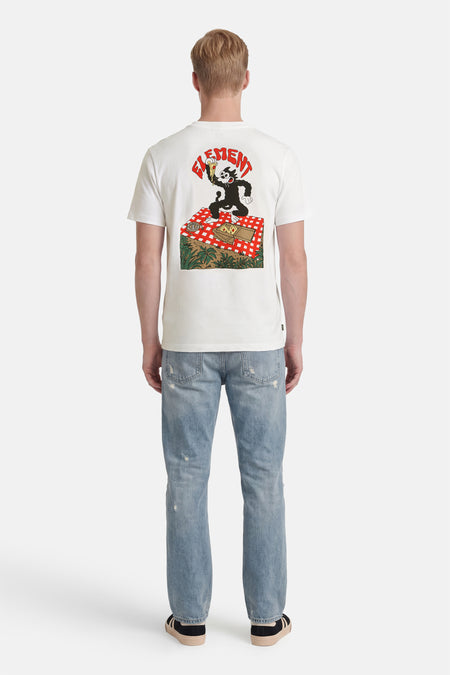 Wit T-shirt van ELEMENT met een opdruk van Felix the Cat op een picknickkleed, gedragen door een man met distressed jeans en sneakers, van achteren gezien.