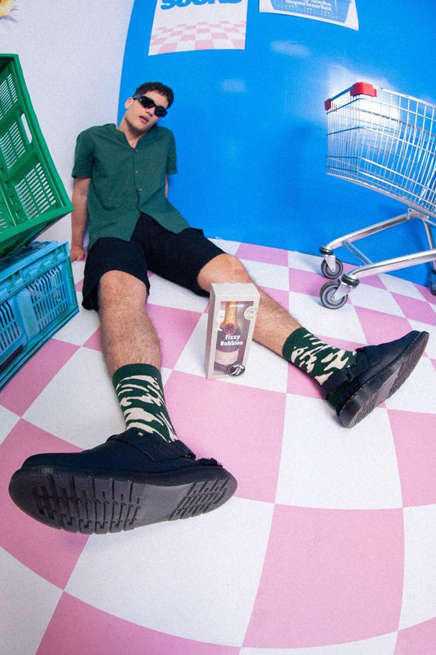 Chaussettes multicolores d'EAT MY SOCKS, avec un motif à carreaux, portées par un modèle avec des short noirs et une blouse verte.