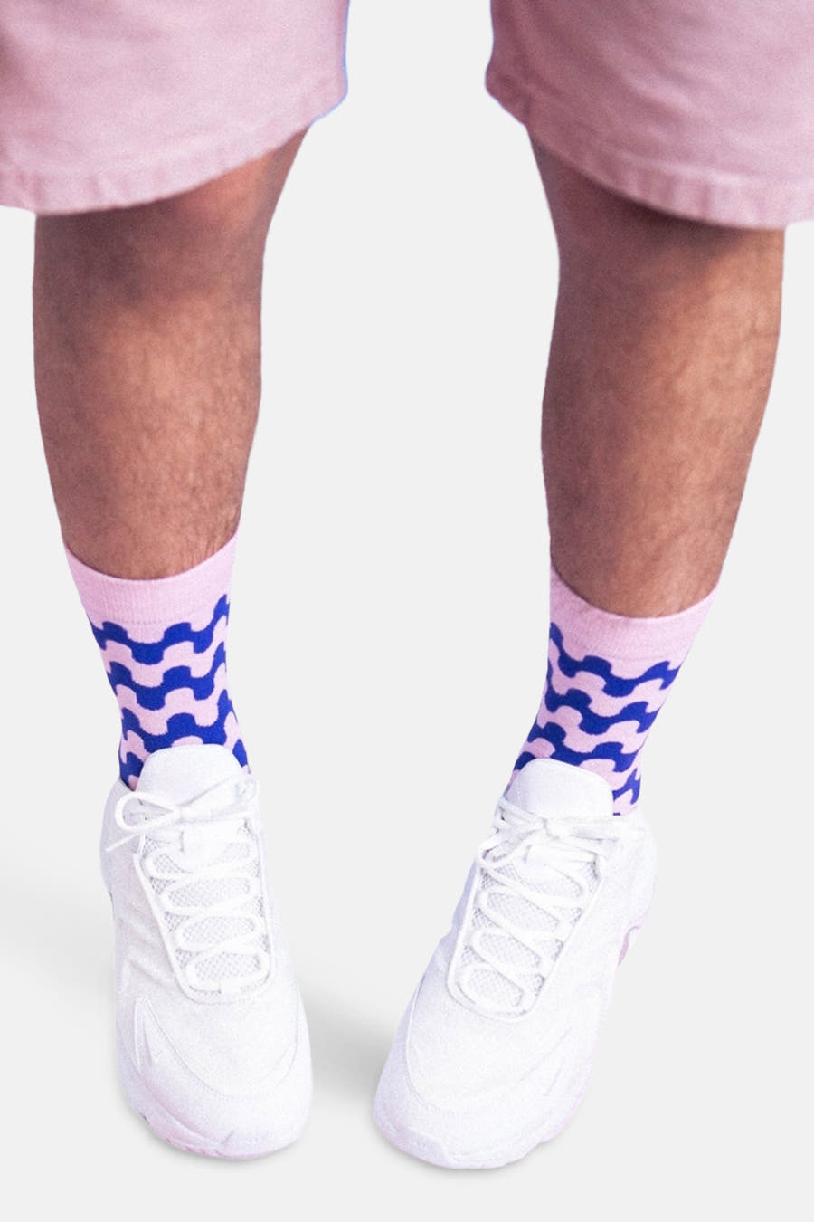 Chaussettes multicolores d'EAT MY SOCKS, avec un motif de vague bleu et des accents roses, portées avec des baskets blanches et des shorts roses.