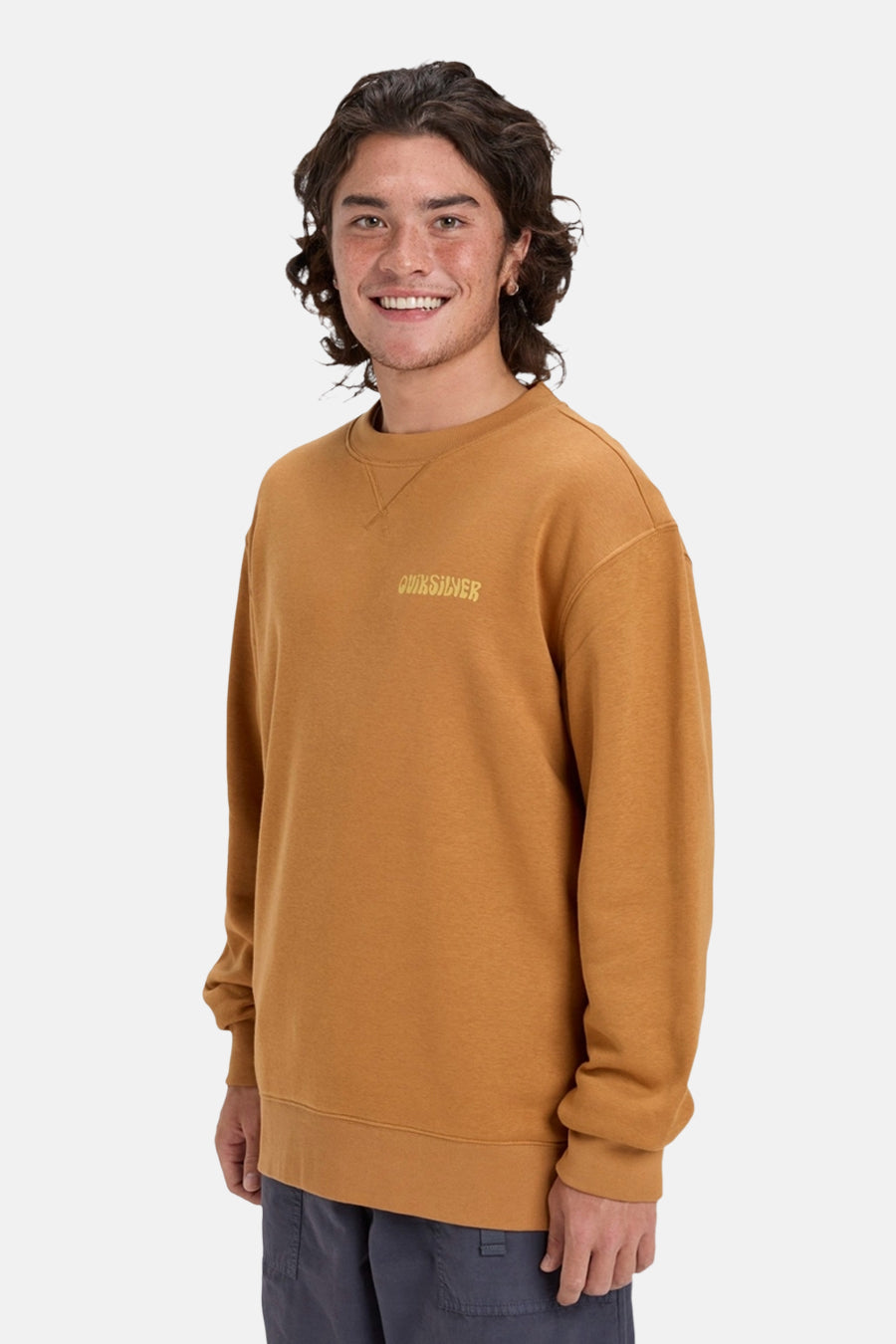 Oranje sweater met ronde hals van Quiksilver, met logo op de borst en grijze broek.
