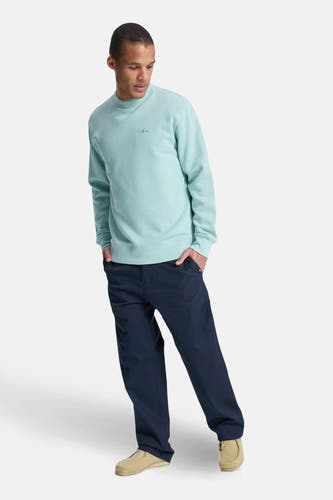 Lichtblauwe sweater van Quiksilver, met lange mouwen en een ronde hals, gecombineerd met een donkere broek en suède schoenen.