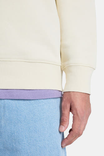 Pull écru de Quiksilver, à manches longues et ourlet côtelé, porté avec un t-shirt lilas et un jean bleu clair.