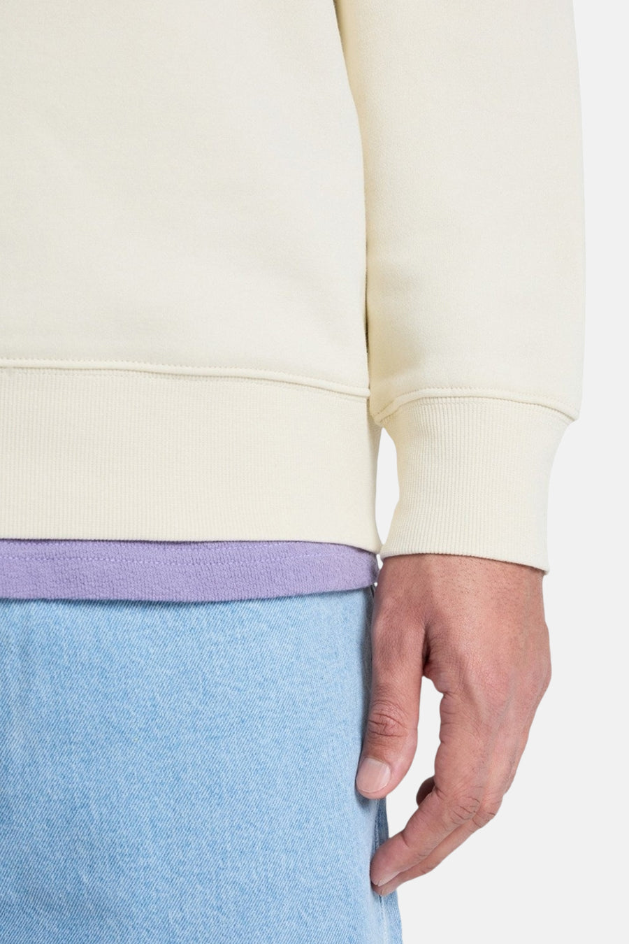 Pull écru de Quiksilver, à manches longues et ourlet côtelé, porté avec un t-shirt lilas et un jean bleu clair.