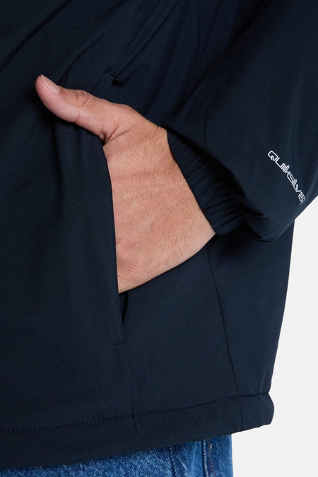 Zwarte korte jas van Quiksilver, met een hand in de zak en het logo op de mouw.
