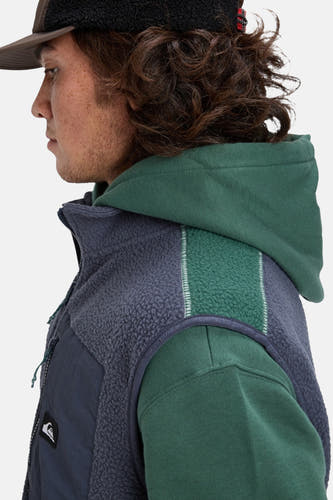 Gilet Quiksilver de couleur bleue avec une texture en polaire et un hoodie vert en dessous.