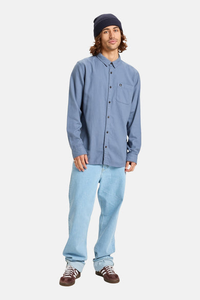 Chemise bleue à manches longues de Quiksilver, avec poche poitrine et portée avec un chapeau et des jeans.