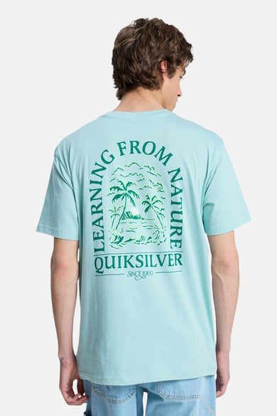 T-shirt bleu de Quiksilver, avec un imprimé vert de palmiers et le texte "Learning from Nature" dans le dos.
