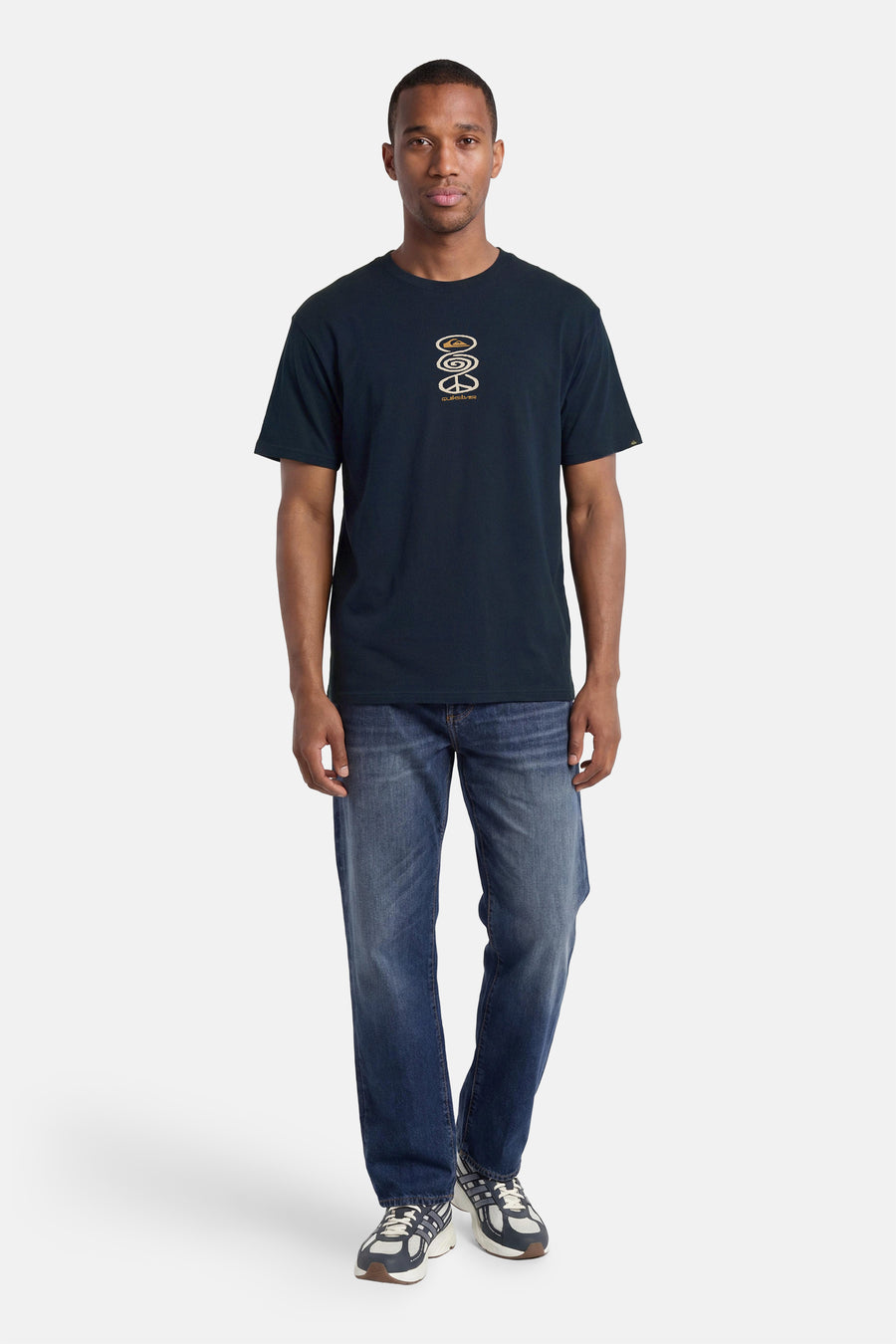 T-shirt à manches courtes bleu foncé Quiksilver, avec un imprimé graphique de couleur or et porté par un homme en jean et baskets.