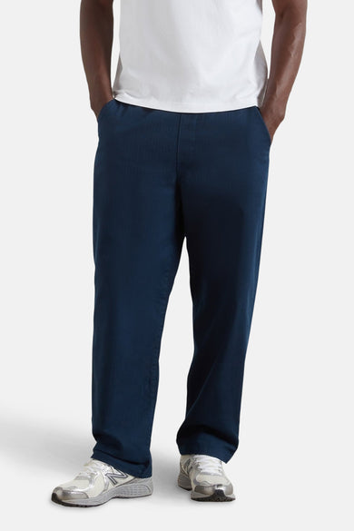 Pantalon bleu de FARAH, avec une ceinture élastique et porté avec des baskets blanches.