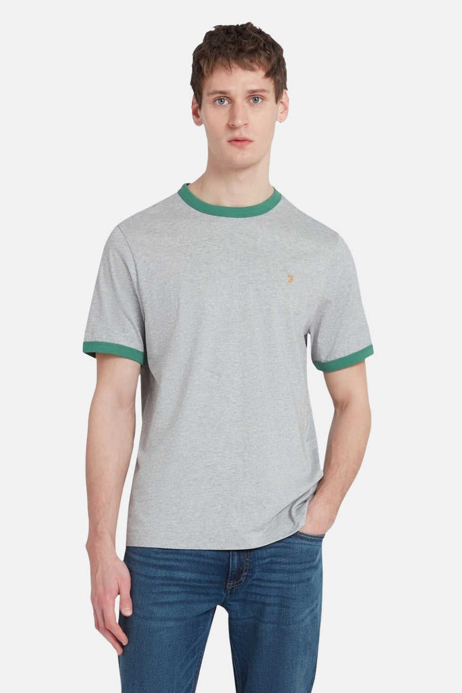 Een man in een grijze T-shirt met groene randen en blauwe jeans.