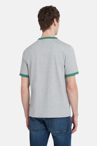 Achterkant van een man in een grijs T-shirt met groene boorden en blauwe jeans.