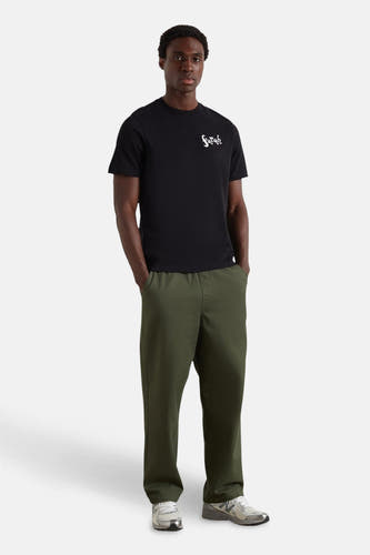 Zwart T-shirt met korte mouwen van FARAH, met witte tekstprint op de borst, gecombineerd met een groene broek en grijze sneakers.
