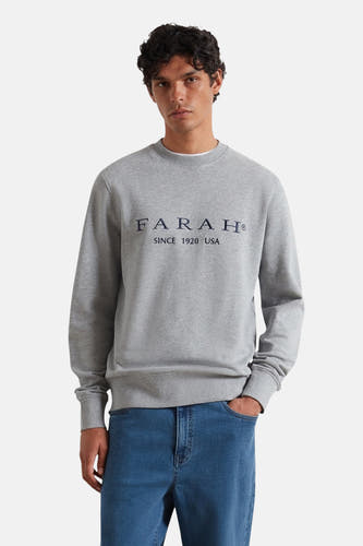 Grijze sweater met ronde hals van FARAH, met logo op de borst, gedragen met blauwe jeans.
