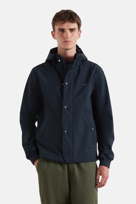 Manteau court bleu de FARAH, avec capuche et fermeture à boutons, porté sur un pantalon vert.