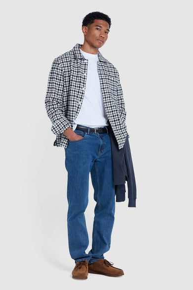 Staande man in geruit overhemd, wit T-shirt en blauwe jeans.