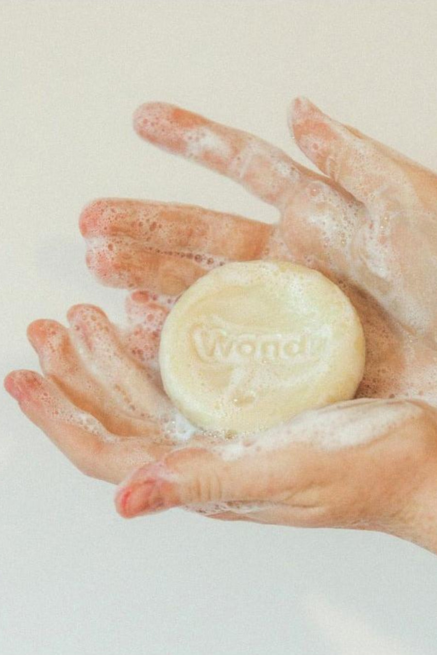 Ronde, crèmekleurige verzorgingsreep van WONDR CARE, gehouden in befoamde handen.
