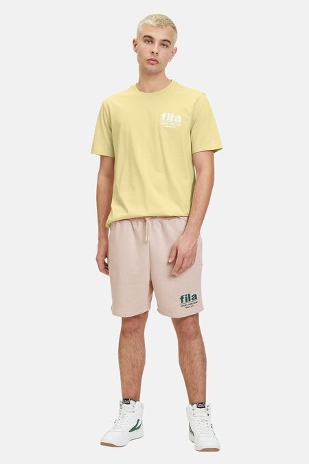 Geel T-shirt met korte mouwen van FILA, met witte print op de borst, gecombineerd met roze shorts en witte sneakers.