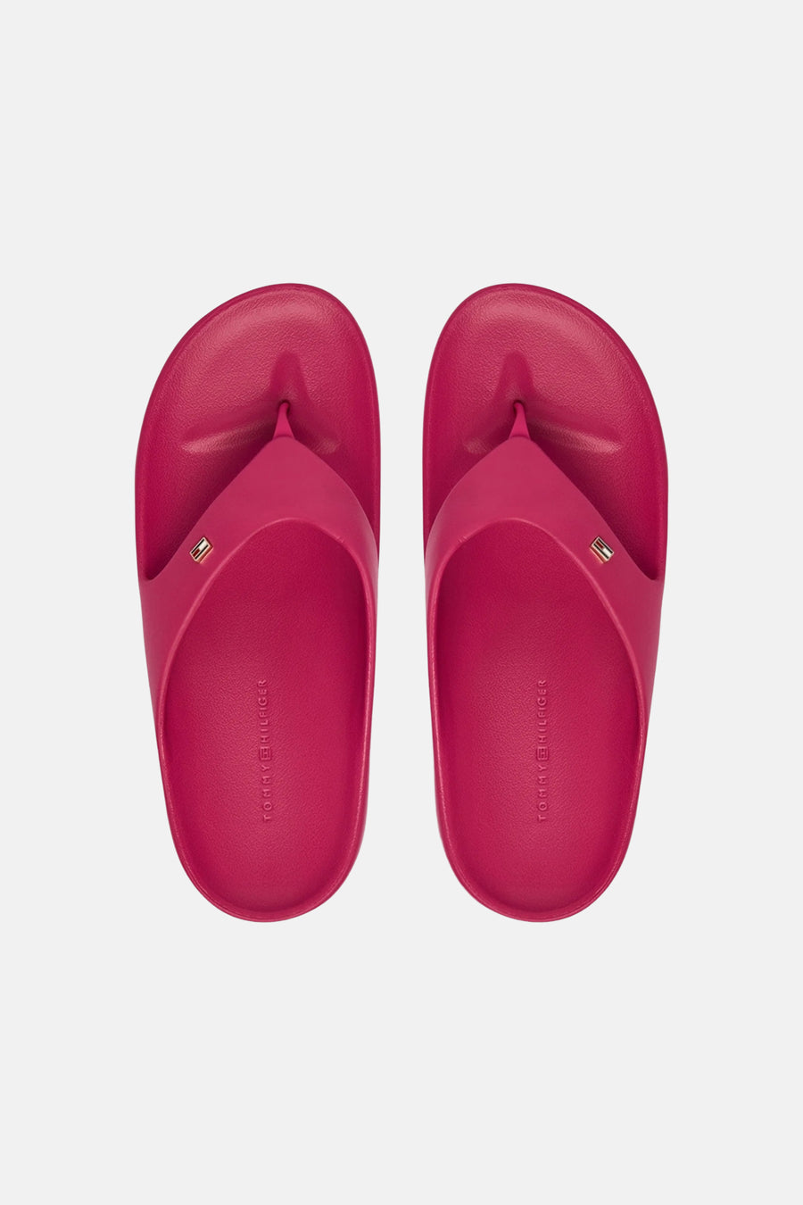 Roze slippers van TOMMY JEANS met een klein logo op de band en merknaam in reliëf op de binnenzool, van bovenaf gezien.