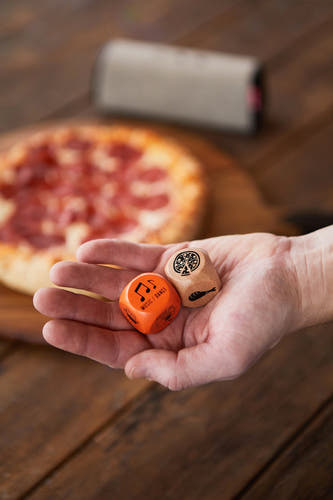 Veelkleurig dobbelstenenset 'geschenk' van Gentlemen's Hardware, met pizza en speaker op een houten tafel.