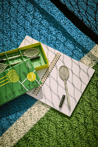 Groene tennispen met racketontwerp van Gentlemen's Hardware, op open notitieboekje op tennisbaan, lifestyle shot