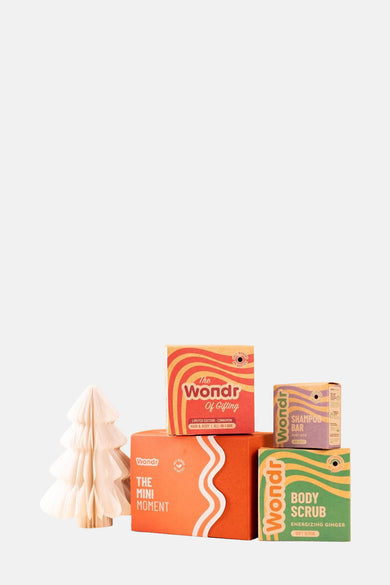 Multicolor geschenkartikel van WONDR CARE, gestapeld met een decoratieve papieren kerstboom aan de zijkant.
