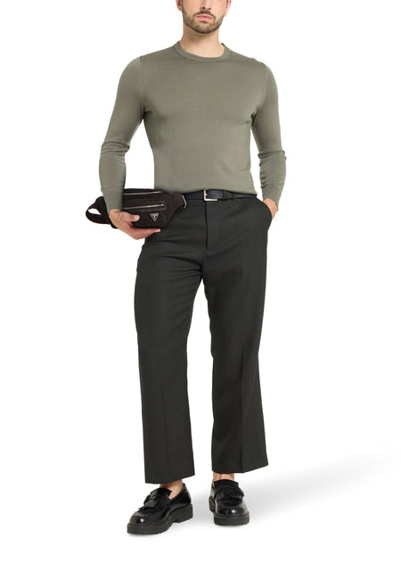 Man met olijfgroene trui, geruite broek, zwarte riem, en zwarte loafers, met een zwarte heuptas.