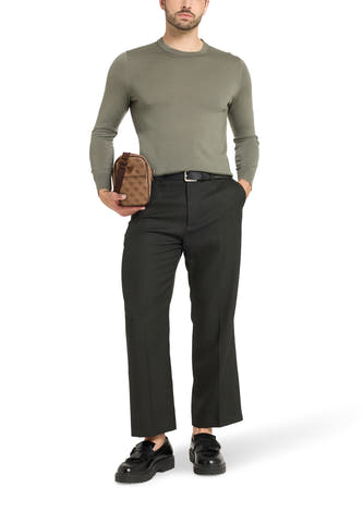 Bruine schoudertas van Guess, met een logo-patroon, gedragen door een model met pantalon en trui.