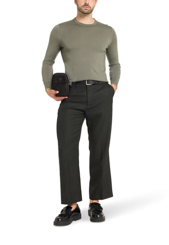 Zwarte schoudertas van Guess, gedragen met een groene trui, grijze broek en zwarte loafers.

