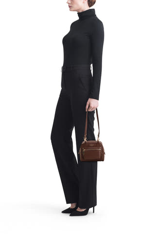 Bruine schoudertas van Guess, klein model met ritsvak, zijwaarts gedragen door een model in het zwart.