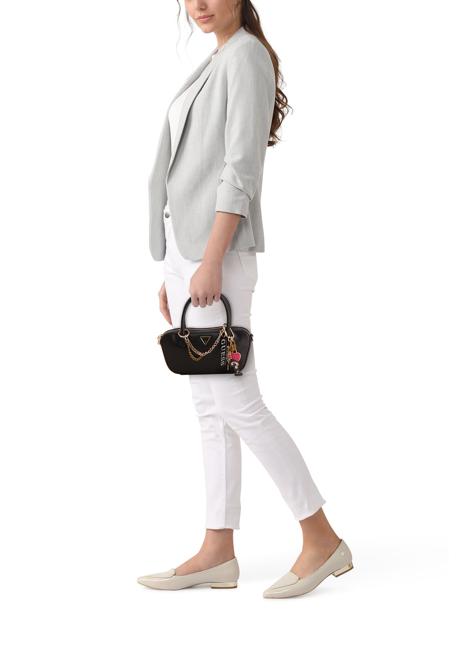 Zwarte handtas van Guess, met gouden details en bedeltjes, gedragen met een grijze blazer en witte broek.
