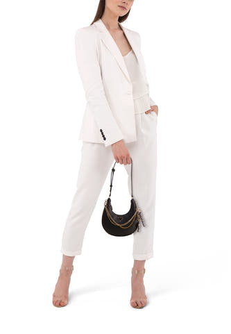 Zwarte schoudertas van Guess, met gouden kettingdetail, gedragen bij een witte broekpak en transparante hakken.
