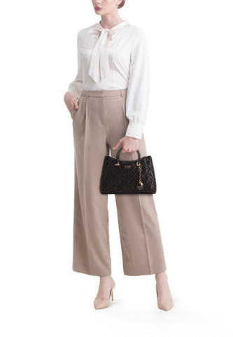 Sac à main noir de Guess avec un motif brodé et des détails dorés, porté par un modèle avec un pantalon beige et une blouse.