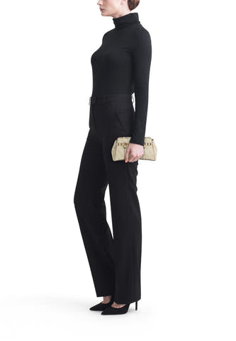 Sac à bandoulière vert Guess, avec quincaillerie dorée et un motif subtil, porté avec un col roulé noir et un pantalon.