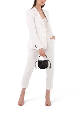 Sac à main noir de Guess, avec des rayures, porté par un modèle en blazer blanc et pantalon.