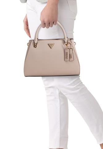 Sac à main beige de Guess, avec détails dorés et breloques logo, porté avec un pantalon blanc.