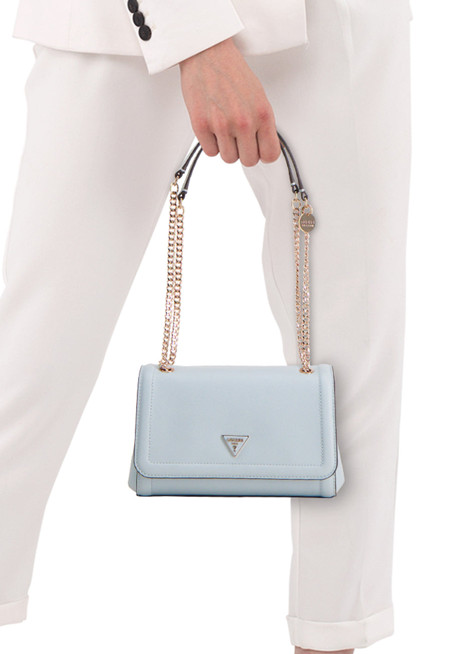 Sac à bandoulière bleu Guess, avec chaîne dorée et logo visible, porté par une personne en pantalon blanc et blazer.