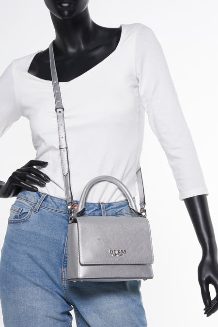 Zilverkleurige handtas van Guess, met korte handgreep en verstelbare schouderriem, gedragen door een mannequin met jeans en wit shirt.
