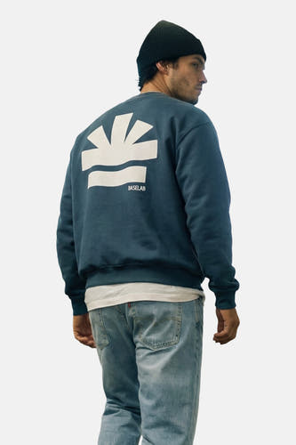 Pull bleu de BASELAB, avec logo blanc dans le dos, porté avec un jean et un bonnet noir.