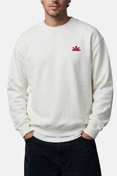Pull blanc à col rond de BASELAB, avec un petit logo rouge sur la poitrine, combiné avec un jean noir.