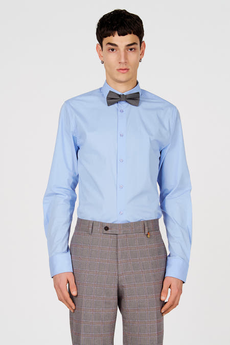 Chemise bleue à manches longues de Le Fabuleux Marcel de Bruxelles, avec fermeture boutonnée, portée avec un pantalon à carreaux et un nœud papillon.