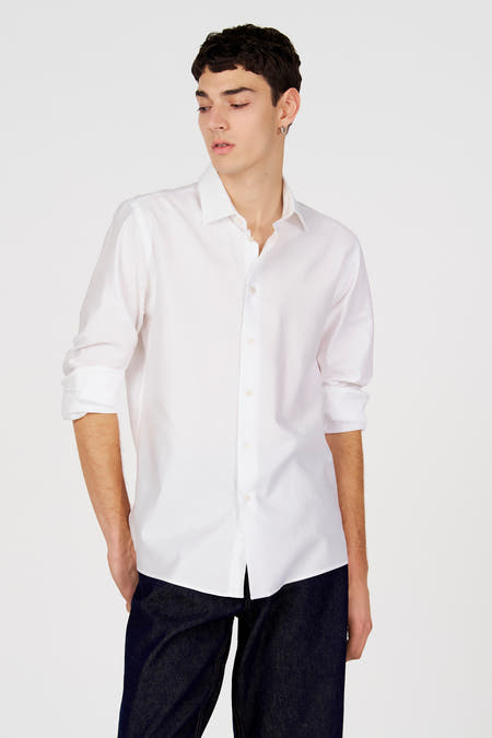 Chemise blanche à manches longues de Le Fabuleux Marcel de Bruxelles, portée avec un jean foncé.