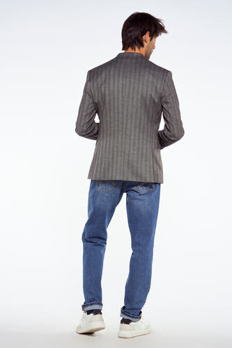 Blauwe blazer van Le Fabuleux Marcel de Bruxelles, met een gestreept patroon, gecombineerd met jeans en witte sneakers, gezien van achteren.
