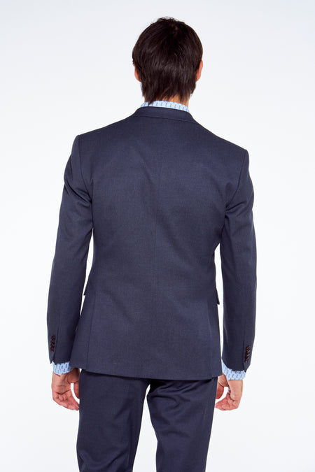 Donkerblauwe blazer van Le Fabuleux Marcel de Bruxelles, achterkant met centrale rits en donkere knopen aan mouwen, gedragen met gestreept overhemd.