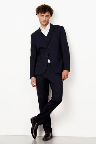 Blazer bleu de Le Fabuleux Marcel de Bruxelles, associé à un gilet coordonné et une blouse blanche, porté avec des chaussures marrons.