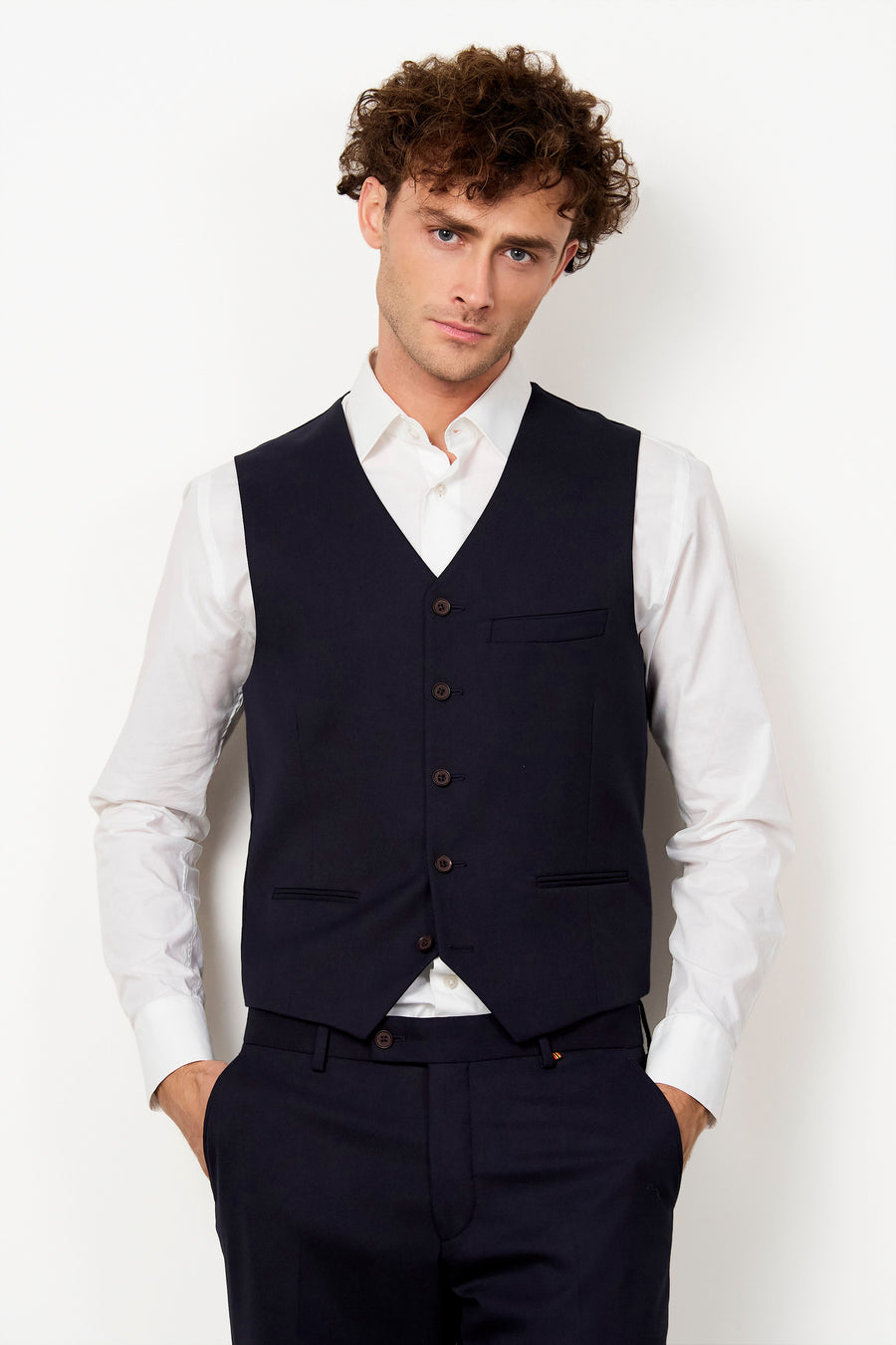 Gilet bleu marine de Le Fabuleux Marcel de Bruxelles avec boutons marron, porté sur une chemise blanche et un pantalon assorti.