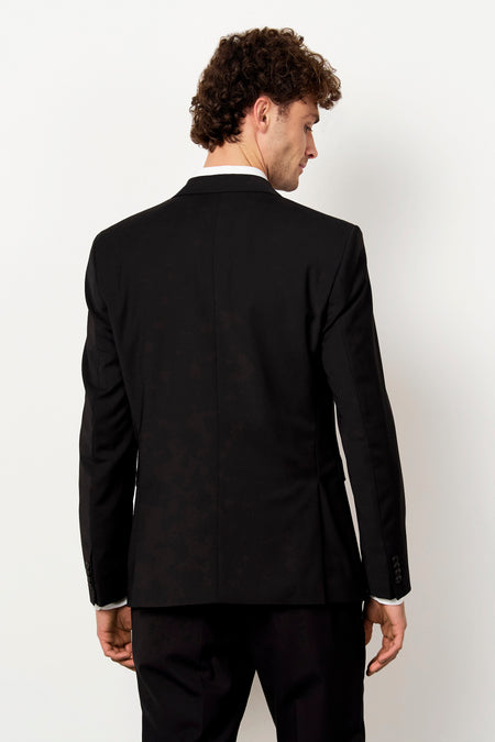 Zwarte blazer van Le Fabuleux Marcel de Bruxelles, van achteren gezien op een man met krullend haar.
