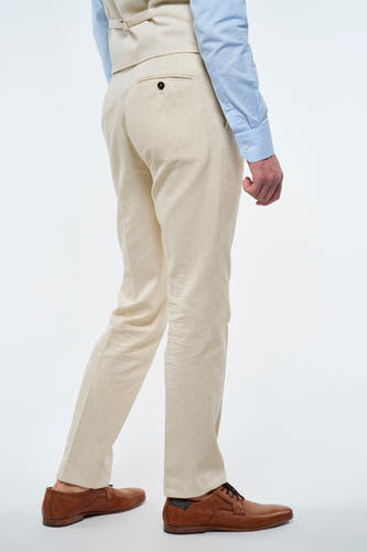 Beige kostuumbroek van Le Fabuleux Marcel de Bruxelles, met een knoopsluiting op de achterzak, gecombineerd met bruine leren schoenen.
