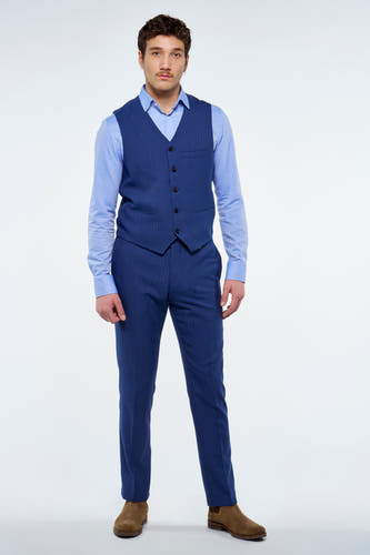 Blauw gilet van Le Fabuleux Marcel de Bruxelles met fijne krijtstreep en donkere knopen, gedragen met een lichtblauw overhemd, bijpassende pantalon en bruine suède laarzen.