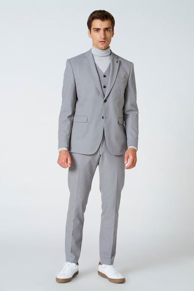 Beige blazer van Le Fabuleux Marcel de Bruxelles, gecombineerd met een grijze coltrui en witte sneakers.
